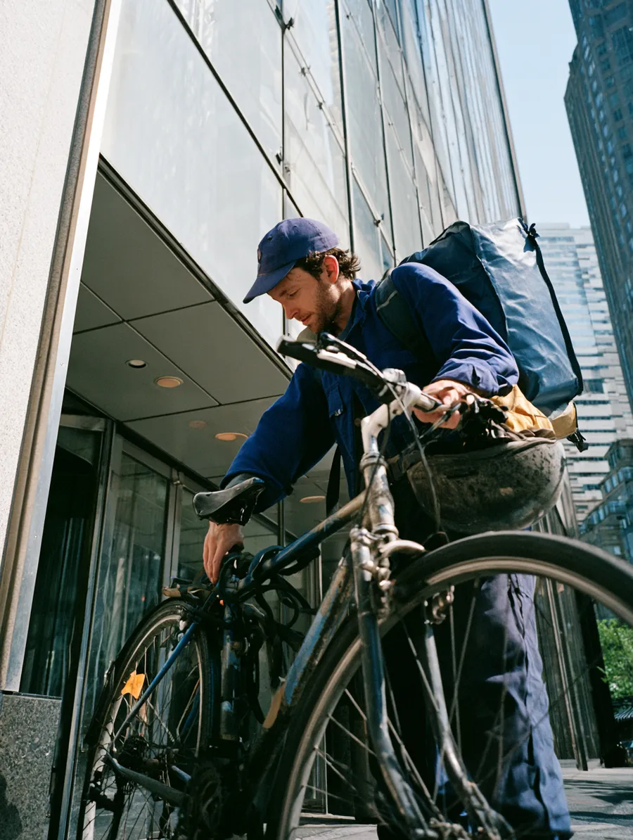 Bike messenger locking up outside an office tower, gig work with predictable seasonal rhythms